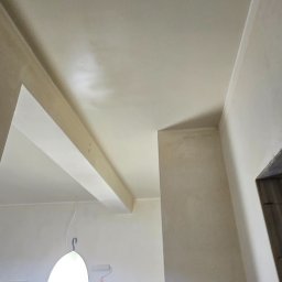 DAMAX Remonty i Wykończenia Wnętrz Damian Mruk - Świeżo pomalowany sufit i ściany w jasnym odcieniu, widoczne narzędzia malarskie: wałek na teleskopie i lampa oświetlająca, podkreślająca gładką powierzchnię.