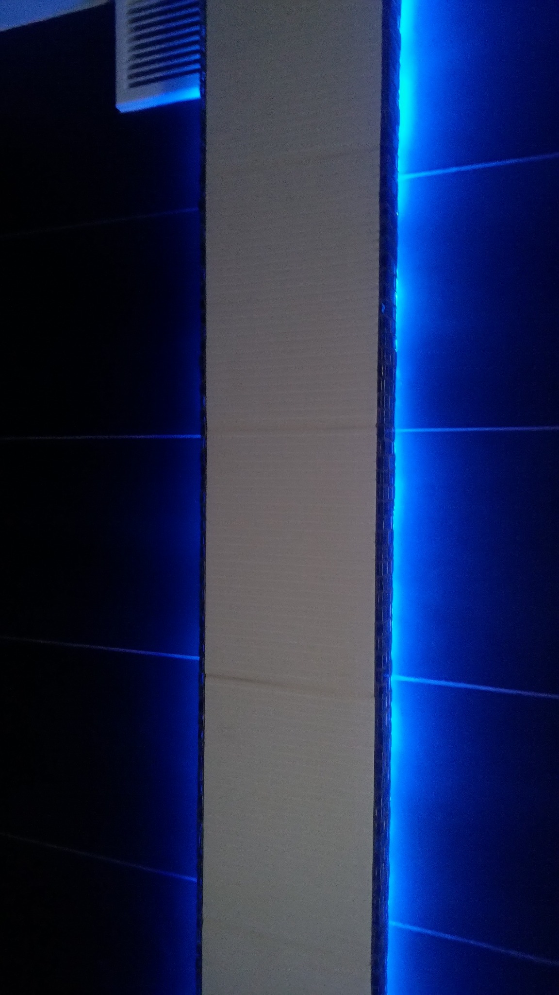 Nowoczesna ściana z podświetleniem LED w odcieniach bieli i głębokiego granatu. Minimalistyczny design z wyraźnymi liniami i subtelnym oświetleniem.