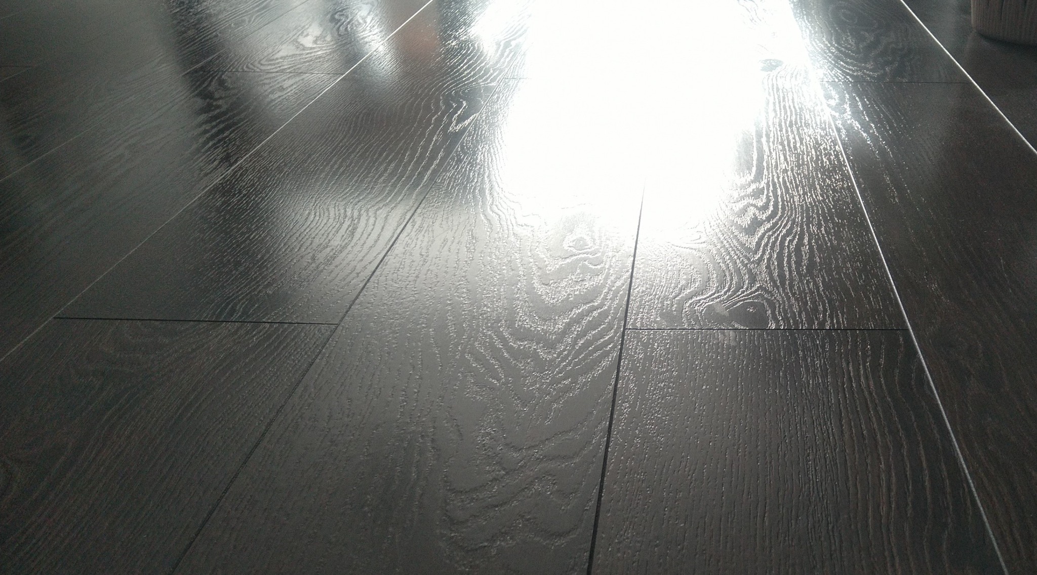 Połyskująca, ciemna podłoga z paneli z wyraźnym rysunkiem drewna, oświetlona padającym światłem, ukazująca precyzję ułożenia i estetyczny wygląd.