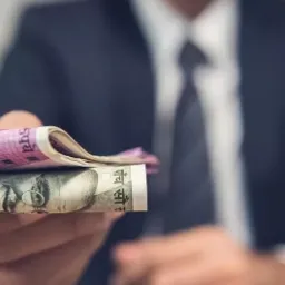 Mężczyzna w garniturze oferuje zwitek banknotów indyjskich rupii o nominałach 500 i 2000.