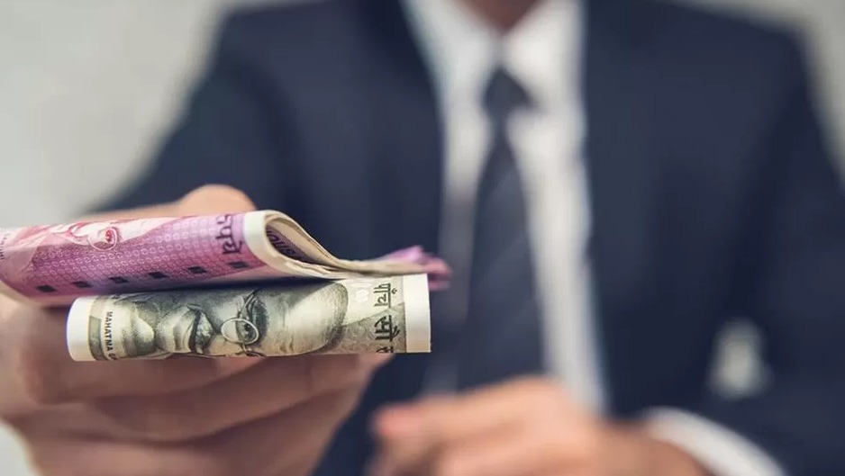 Mężczyzna w garniturze oferuje zwitek banknotów indyjskich rupii o nominałach 500 i 2000.