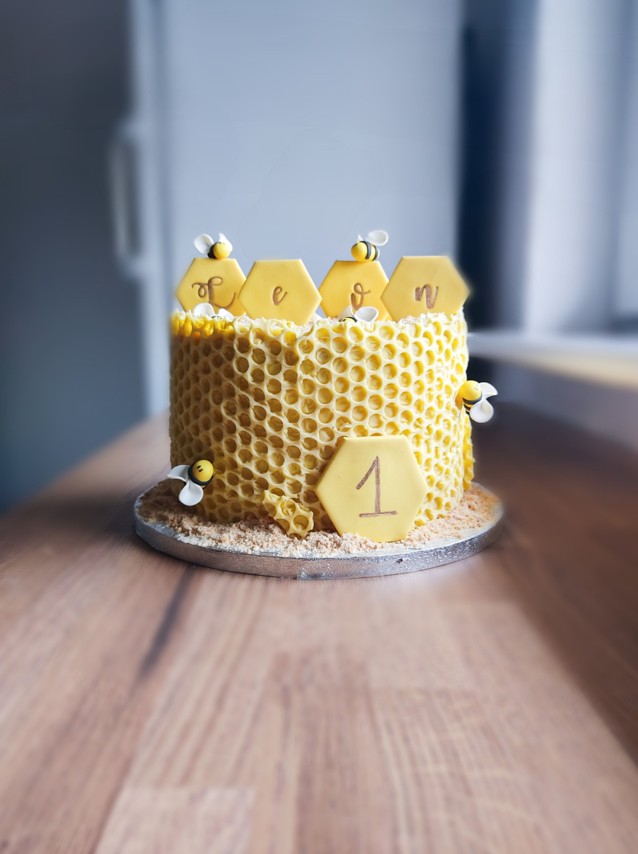 Tort w kształcie plastra miodu z dekoracjami pszczół i napisem 'One' na drewnianym stole.
