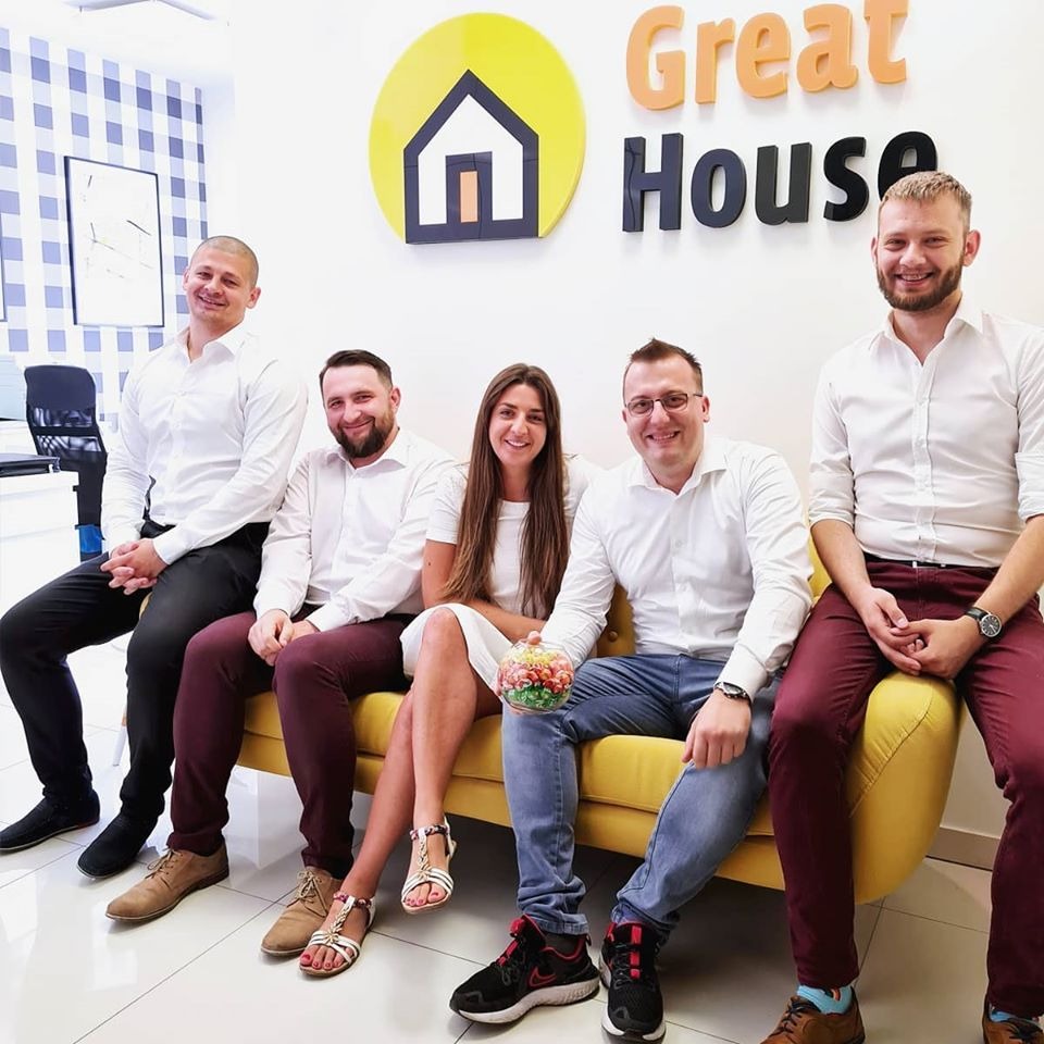 Zespół pracowników firmy 'Great House' ze Staszowa siedzi na żółtej kanapie przed ścianą z logo firmy i niebieską tapetą w kratkę.