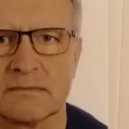 Portret mężczyzny w okularach, z poważnym wyrazem twarzy, na jasnym tle.