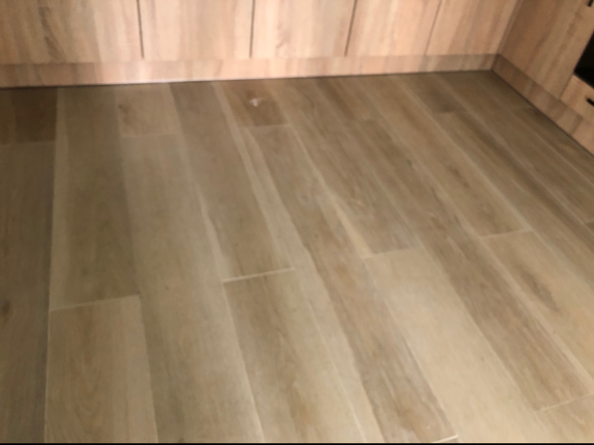 Ułożone panele podłogowe w odcieniach beżu, widoczne łączenia i struktura drewna, przy ścianie zabudowa meblowa.