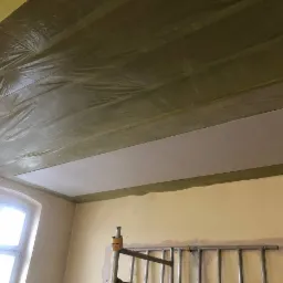 Montaż izolacji poddasza z widoczną folią paroizolacyjną i częściowo zamontowaną płytą gipsowo-kartonową, widoczny fragment drabiny.