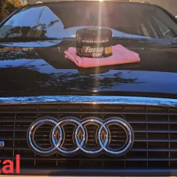 Czarny samochód Audi S-Line z nałożonym woskiem Fusso Coat i różową ściereczką z mikrofibry na masce, widok z przodu na grill i reflektory.