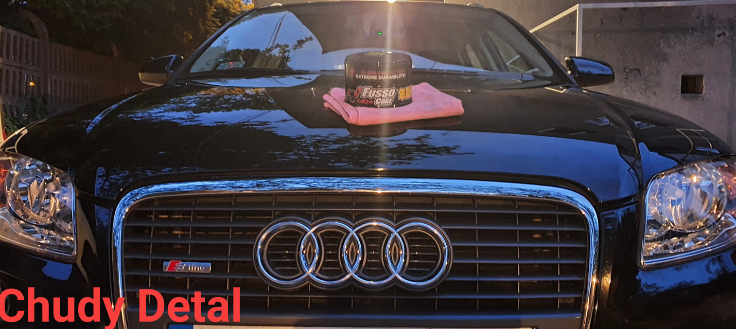 Czarny samochód Audi S-Line z nałożonym woskiem Fusso Coat i różową ściereczką z mikrofibry na masce, widok z przodu na grill i reflektory.