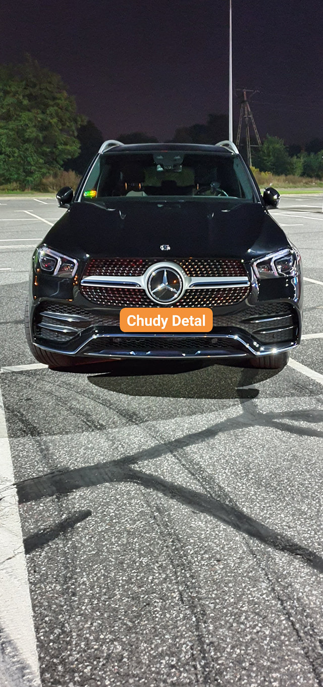 Czarny Mercedes GLE, widok z przodu na parkingu nocą, z widocznym grillem i reflektorami, z efektem mokrej nawierzchni na asfalcie.