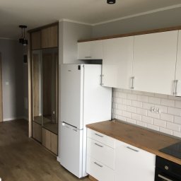 Piotr Głoćko - Nowoczesna kuchnia z białymi szafkami, drewnianym blatem i płytkami typu metro na ścianie, obok szafa wnękowa z lustrzanymi drzwiami i oświetleniem punktowym.