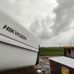 Kamera monitoringu Hikvision na budowie w pochmurny dzień, z widoczną konstrukcją budynku w tle.