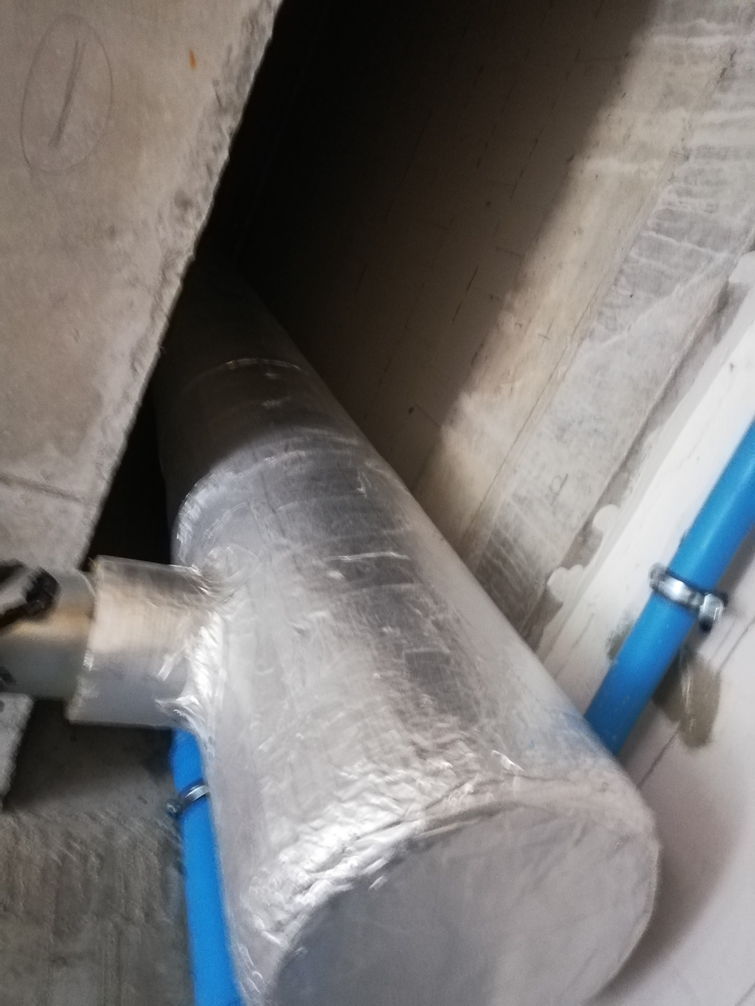 Izolowany przewód wentylacyjny z odgałęzieniem, mocowany do sufitu, z widocznymi niebieskimi rurami i metalowymi opaskami zaciskowymi.