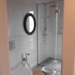 Fest - remonty mieszkań - Nowoczesna łazienka z kabiną prysznicową, toaletą z bidetem i okrągłym lustrem w czarnej ramie. Na podłodze wzorzyste płytki, obok pudełka i miska z wodą.