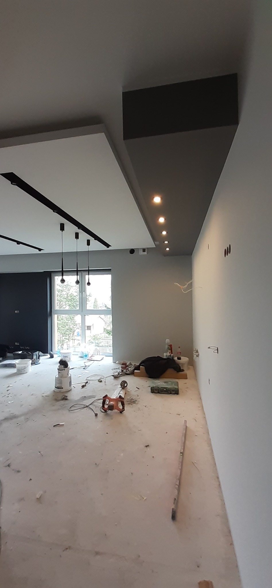 Wnętrze mieszkania w Katowicach w trakcie prac wykończeniowych: widoczne narzędzia, sufit z oświetleniem punktowym i listwami LED, ślady po szpachlowaniu na podłodze.