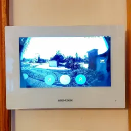 Ekran wideodomofonu Hikvision zamontowanego na ścianie, wyświetlający obraz z kamery zewnętrznej w zimowej scenerii.