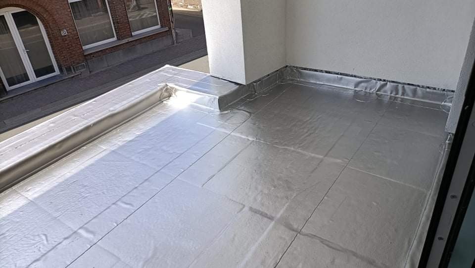 Szczelne krycie dachu płaskiego papą termozgrzewalną z obróbkami blacharskimi przy ścianie budynku mieszkalnego.