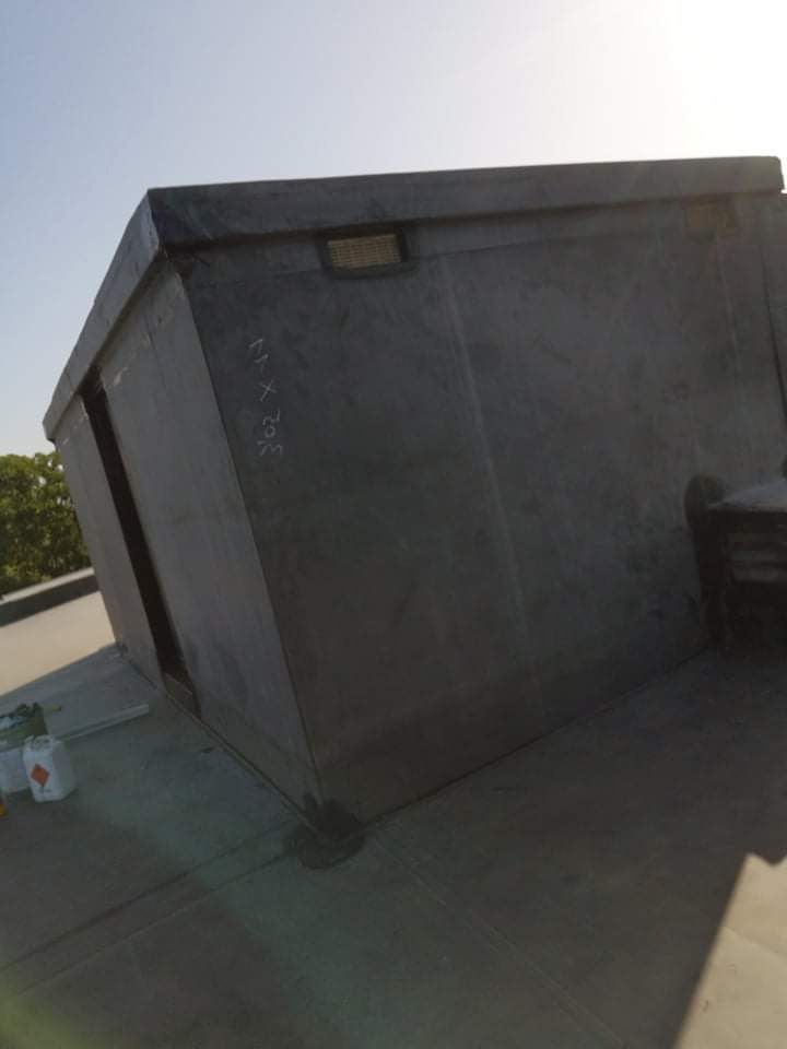 Szare, płaskie zadaszenie na dachu budynku, z widocznymi obróbkami blacharskimi i uszczelnieniami, częściowo w cieniu, z butelkami z płynami w tle.