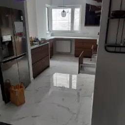 Jasna kuchnia z marmurową podłogą, drewnianymi szafkami i oknem zasłoniętym folią ochronną podczas remontu, z balonami w tle.