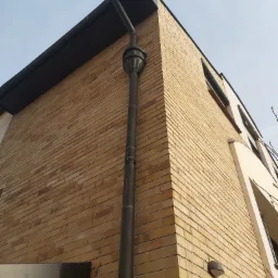 Elewacja budynku z żółtej cegły z systemem odprowadzania wody deszczowej z dachu, ozdobny element na rurze spustowej, widok z dołu na narożnik budynku.