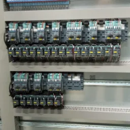 Szczegółowe ujęcie wnętrza szafy sterowniczej z licznymi przekaźnikami, listwami zaciskowymi i okablowaniem, zamontowanymi na szynach DIN.