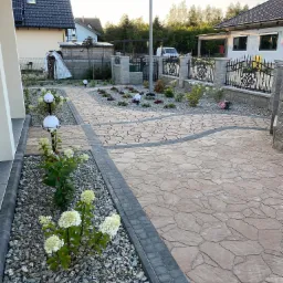 Ogród przydomowy z krętą ścieżką z kamiennej kostki, obrzeżami z szarej kostki, rabatami z białymi hortensjami i kamiennym grysem, oświetlony kulistymi lampami, ogrodzony kutym płotem.