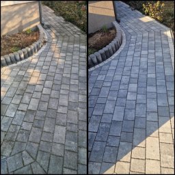 MS SERWIS MATEUSZ STRÓZIK - MYCIE CIŚNIENIOWE - Efekt przed i po czyszczenia kostki brukowej: po lewej stronie widoczny brudny fragment, po prawej - czysta, szara kostka. Widoczne obrzeża i fragment budynku.