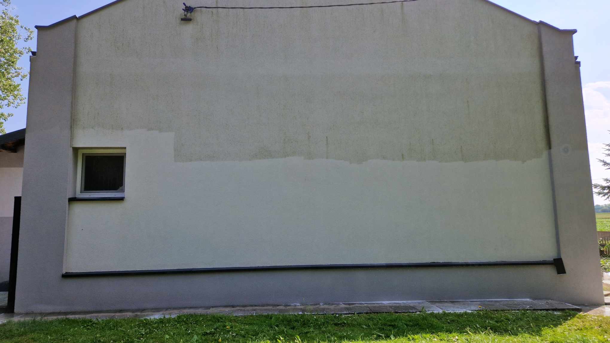 Częściowo umyta, jasna elewacja budynku z widoczną różnicą w czystości, okno po lewej stronie, trawa u dołu. Prezentacja efektu czyszczenia.