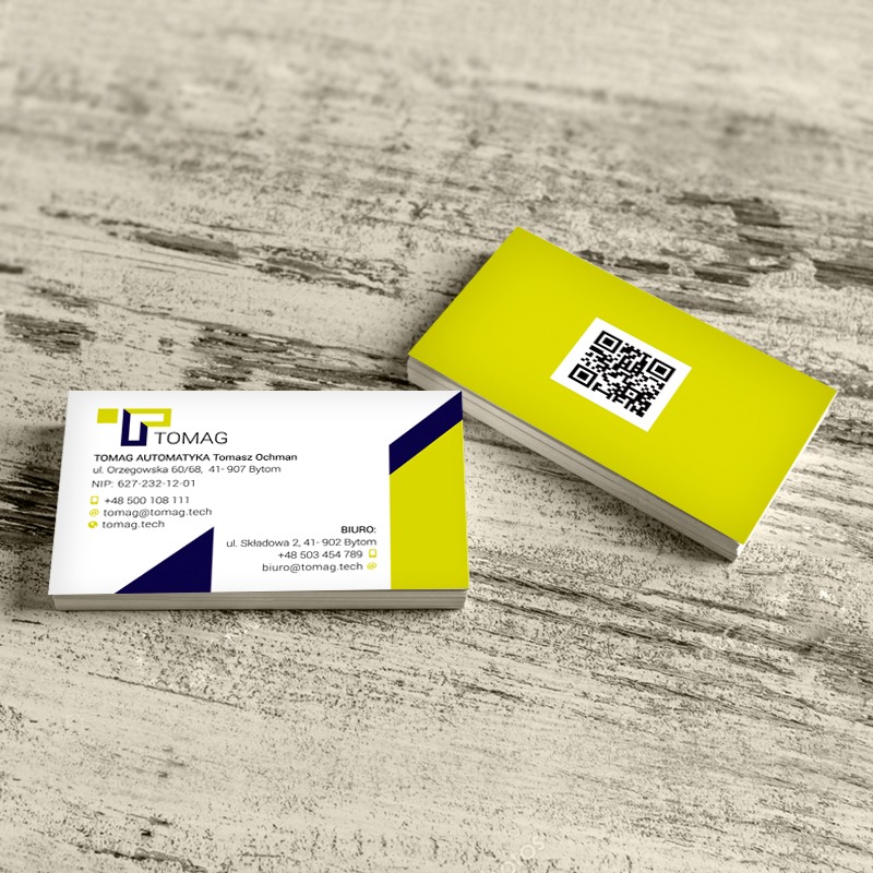 Stos wizytówek firmy TOMAG AUTOMATYKA z kodem QR na limonkowym tle, leżący na drewnianej powierzchni.