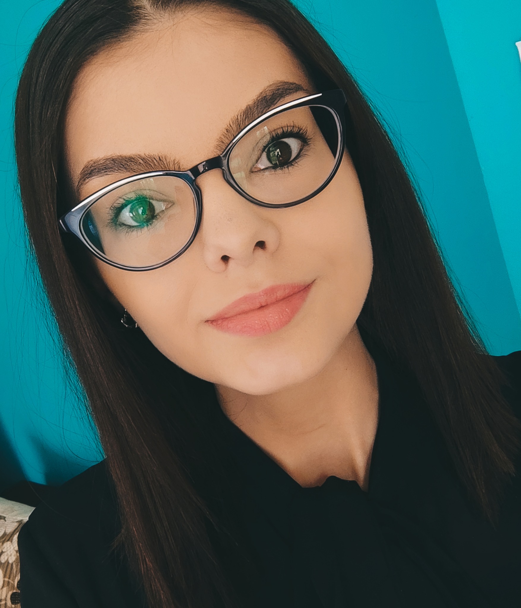 Portret kobiety w okularach z czarno-białymi oprawkami na tle turkusowej ściany.