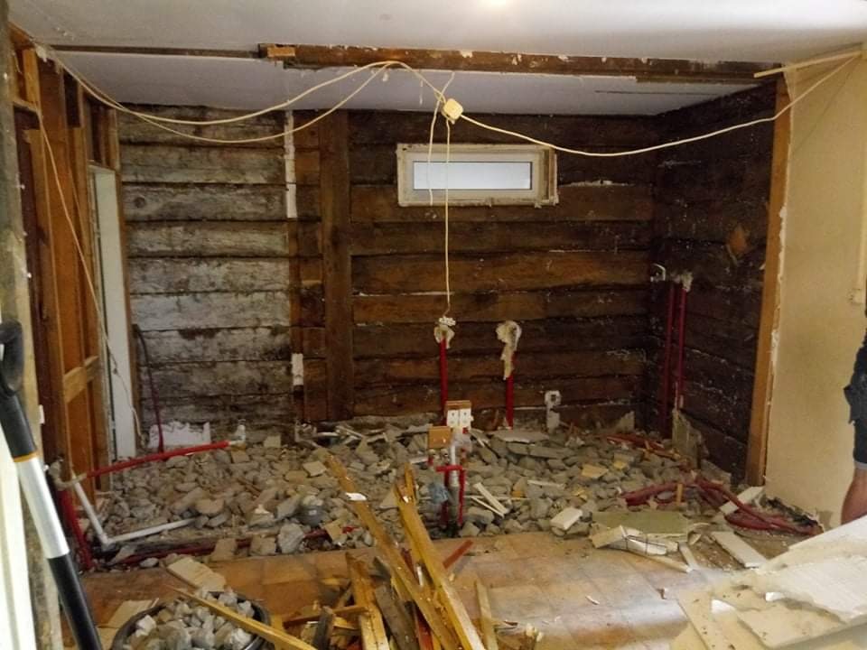 Demontaż starej łazienki: odsłonięte drewniane ściany, gruz na podłodze, widoczne rury instalacyjne