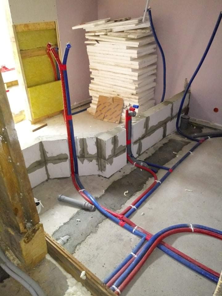 Instalacja wodna z rur PEX w kolorach czerwonym i niebieskim, prowadzona w surowym stanie łazienki, widoczna izolacja z wełny mineralnej w ścianie i bloczki betonowe.