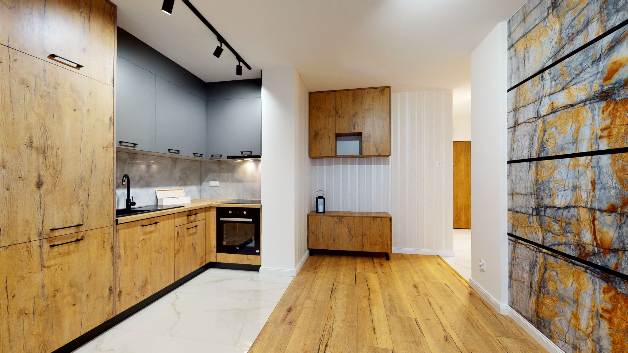 Nowoczesna kuchnia z drewnianymi frontami szafek, szarymi górnymi szafkami i blatem imitującym beton, białą podłogą w strefie roboczej i drewnianą w części jadalnej, oświetleniem punktowym...