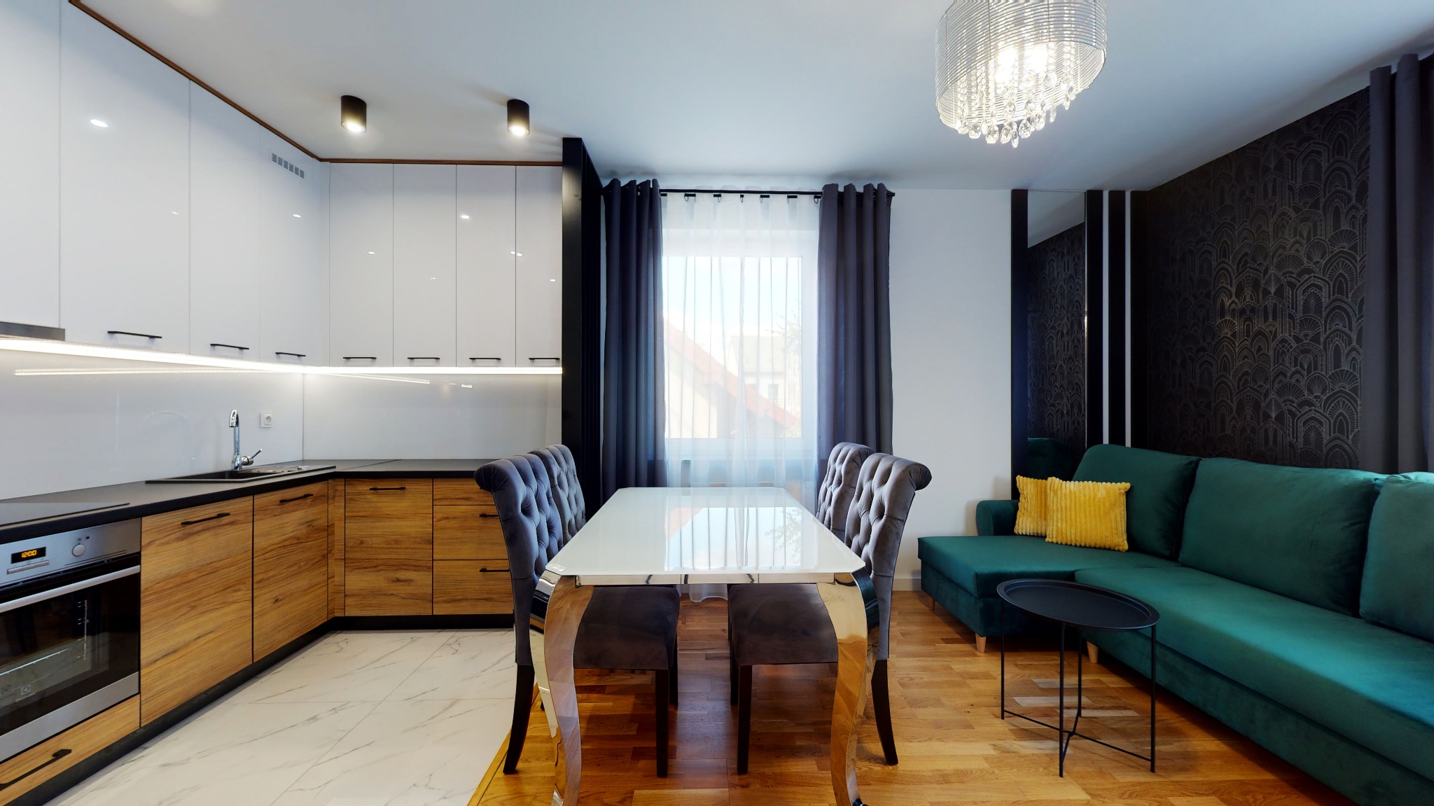 Nowoczesna kuchnia z białymi szafkami i drewnianymi frontami, marmurowa podłoga, stół z krzesłami z aksamitnym obiciem, zielona sofa z żółtymi poduszkami, ozdobny żyrandol i tapeta w stylu art deco.