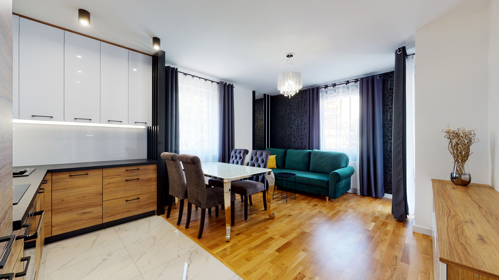Wnętrze mieszkania po remoncie: kuchnia z drewnianymi i białymi szafkami, marmurowa podłoga, stół z krzesłami tapicerowanymi aksamitem, zielona sofa, parkiet i dekoracyjna tapeta.