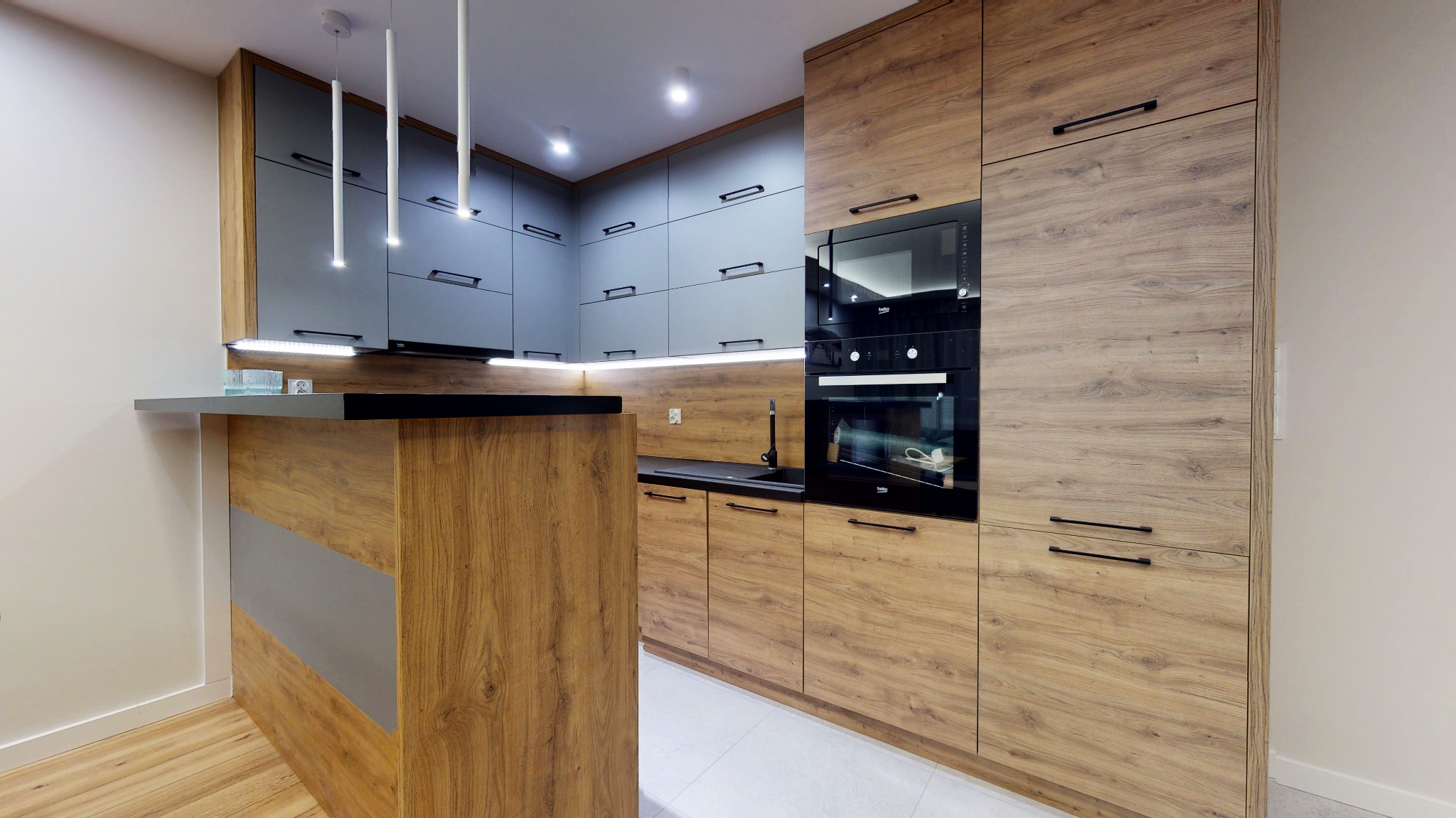 Nowoczesna kuchnia z drewnianymi i szarymi szafkami, czarnym blatem, oświetleniem LED i minimalistycznymi lampami wiszącymi