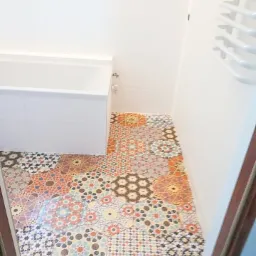 Wnętrze łazienki z wanną i grzejnikiem drabinkowym, wyróżniające się podłogą wyłożoną kolorowymi, heksagonalnymi płytkami o wzorach marokańskich i arabskich, ułożonymi w patchworkowy sposób.