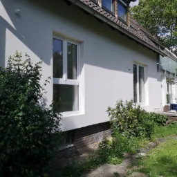 Biała elewacja domu jednorodzinnego z nowymi oknami, widok z boku, zieleń w ogrodzie.