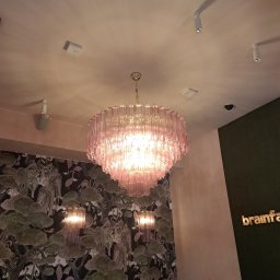 PE - Smart Home - Różowy, kaskadowy żyrandol z prążkowanego szkła, oświetlający wnętrze z wzorzystą tapetą i reflektorami sufitowymi. Widok z dołu.