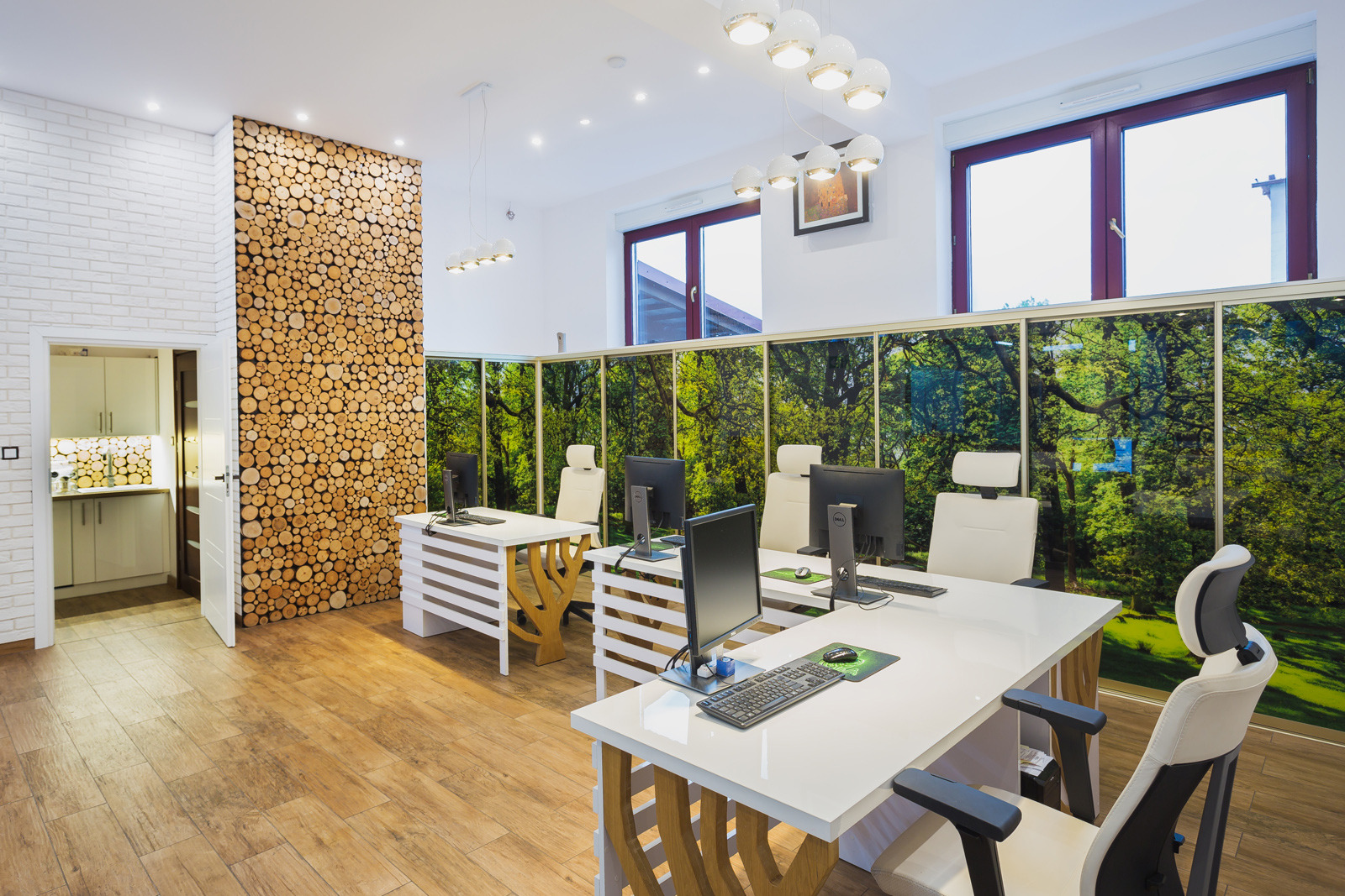 Nowoczesne biuro z drewnianą ścianą z bali, białymi biurkami i fototapetą leśną. Jasne wnętrze z oknami i designerskim oświetleniem.
