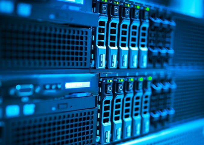Rząd serwerów w szafie rack, z widocznymi dyskami twardymi i diodami LED sygnalizującymi pracę, oświetlonych niebieskim światłem.