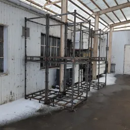 Surowa, metalowa konstrukcja szkieletowa pod halę, widoczna na zewnątrz budynku z fragmentami śniegu, eksponująca spawy i łączenia, pod zadaszeniem z blachy falistej.