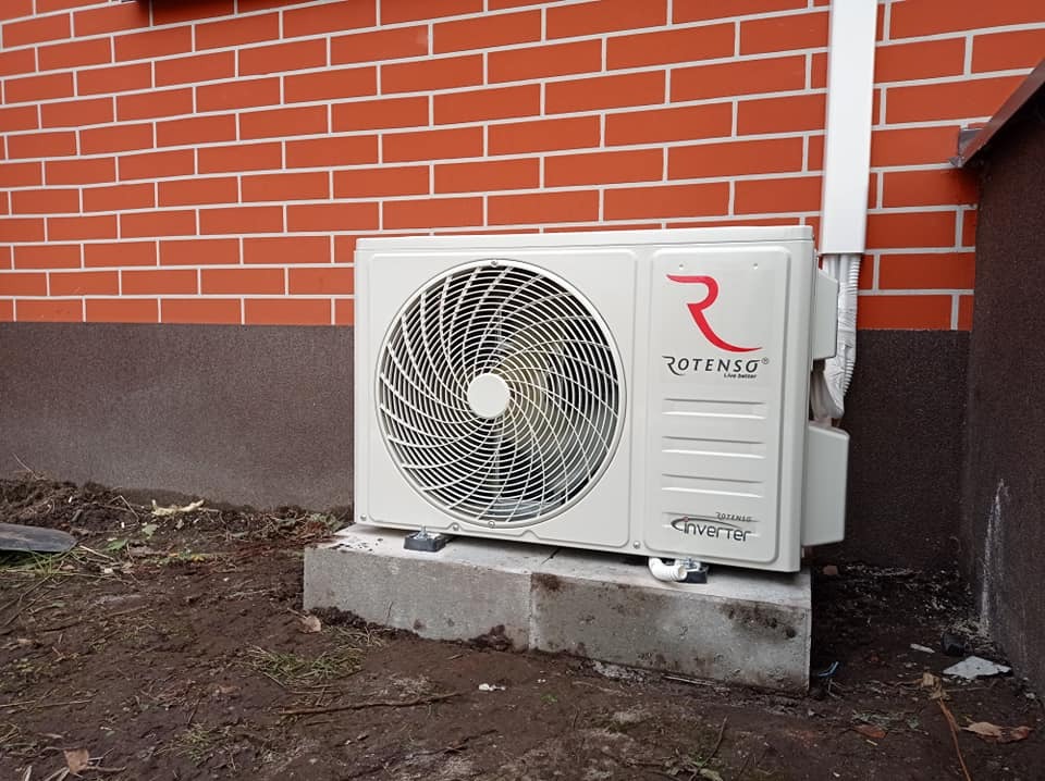 Zewnętrzna jednostka klimatyzacji Rotenso Inverter zamontowana na betonowym fundamencie przy ceglanej ścianie budynku.