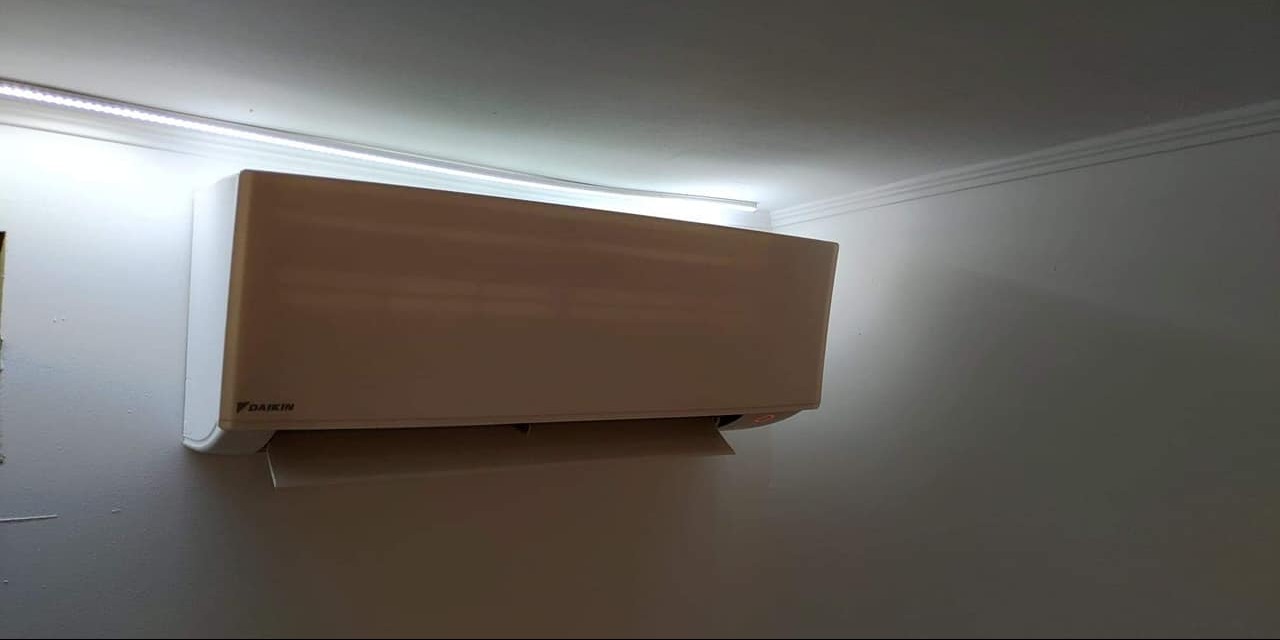 Klimatyzator Daikin zamontowany na ścianie, oświetlony listwą LED, widoczne logo producenta.