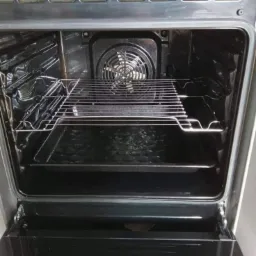 Wnętrze otwartego piekarnika z widoczną grzałką i kratką, po procesie czyszczenia, z lekkimi zaciekami na dnie.