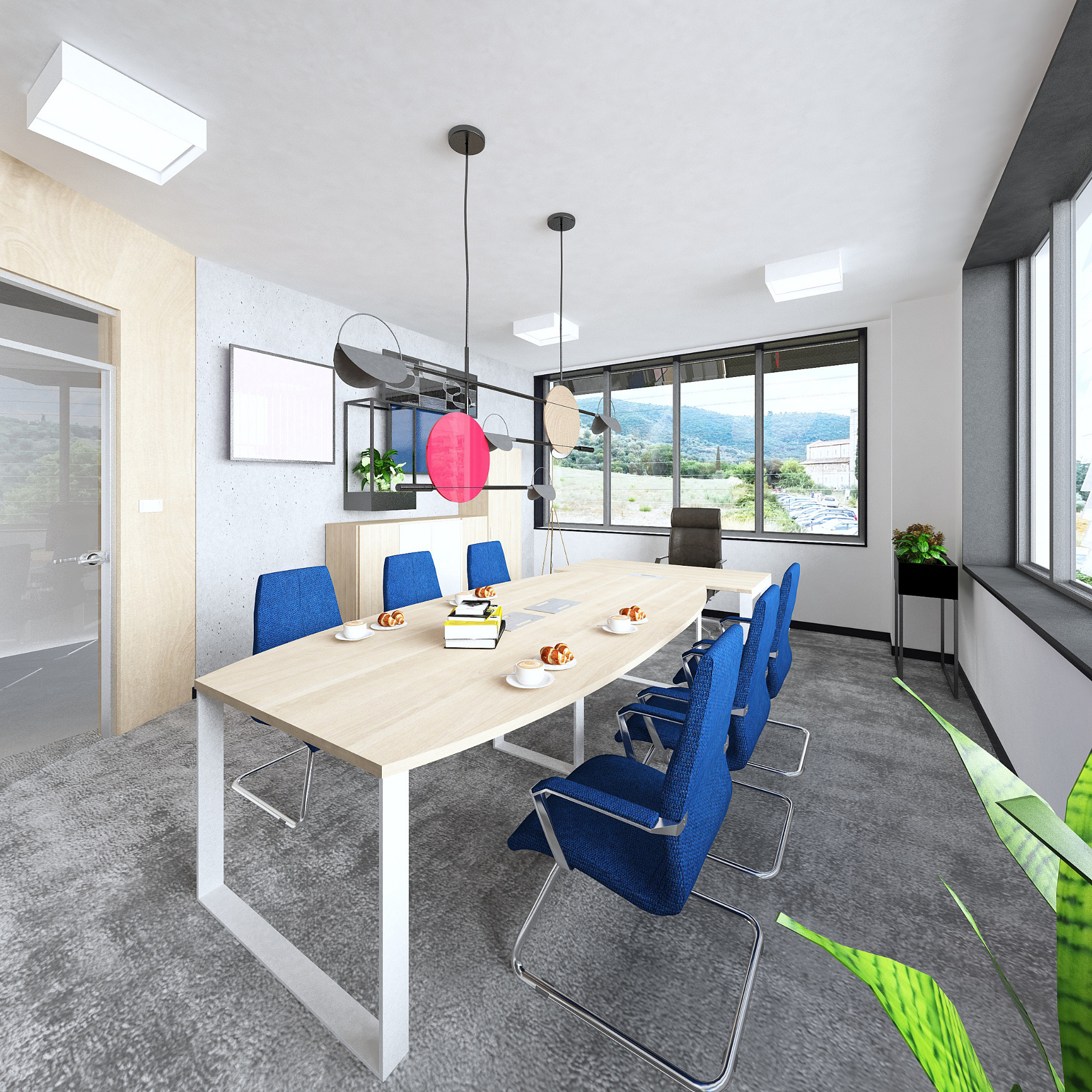 Nowoczesna sala konferencyjna z dużym stołem z jasnego drewna, niebieskimi krzesłami i widokiem na góry za oknem; na stole leżą książki, filiżanki i rogaliki.