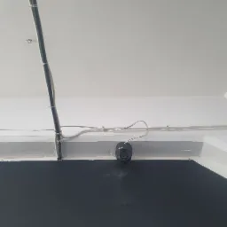 Kamera monitoringu BCS zamontowana pod sufitem, widoczne okablowanie i listwy mocujące. Ujęcie od dołu, na tle czarnej ściany.