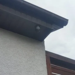 Kamera monitoringu kopułkowa, zainstalowana pod okapem budynku w Kostrzynie nad Odrą, widoczna z niskiego kąta, z fragmentem drewnianej konstrukcji w tle.