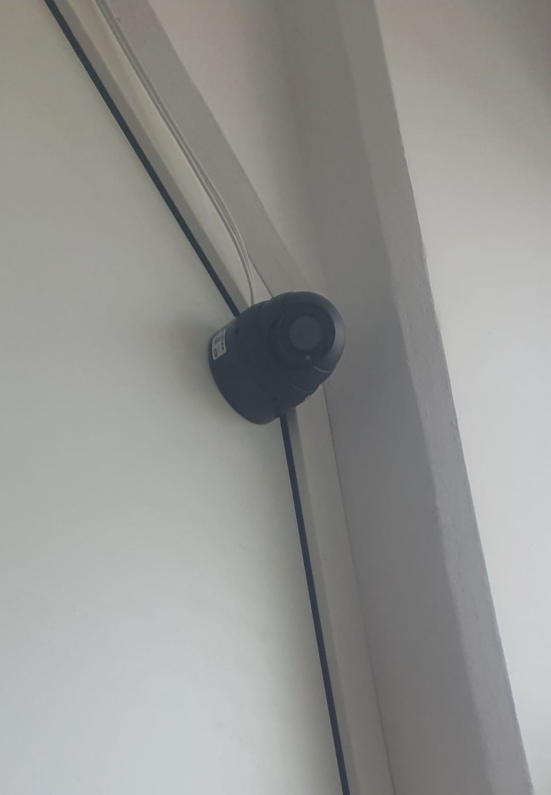 Kopułkowa kamera monitoringu CCTV, zamontowana na białej ścianie, widok z dołu, widoczne przewody.