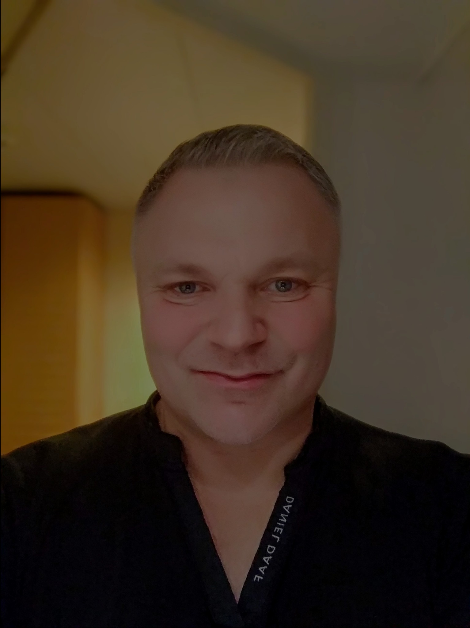 Portret mężczyzny w czarnej koszuli z wyhaftowanym imieniem i nazwiskiem DANIEL DAAG.