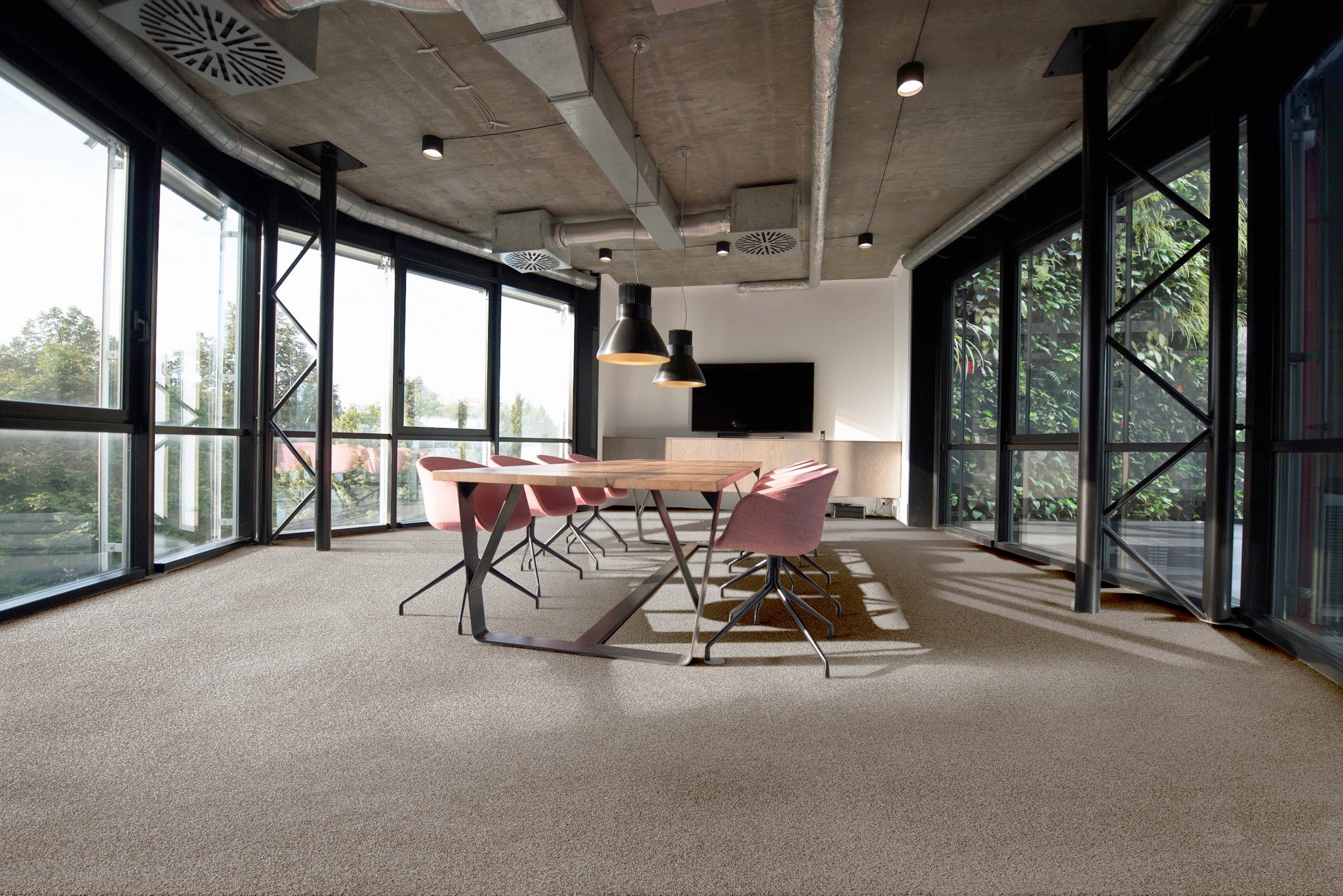 Jasnoszara podłoga w nowoczesnym biurze z dużymi oknami, drewnianym stołem i różowymi krzesłami na metalowych nogach, widoczne elementy wentylacji pod sufitem.